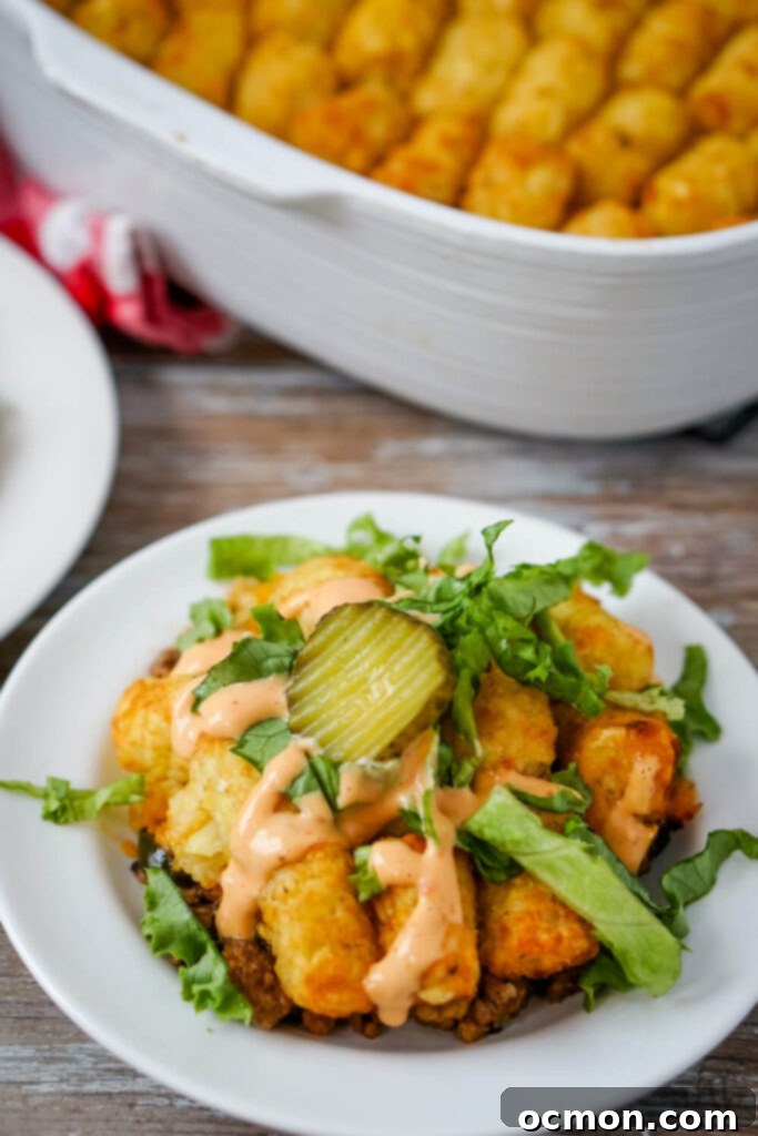 Loaded Big Mac Tater Tot Bake 3 A serving of Big Mac Tater Tot Casserole topped with freshly shredded lettuce, thousand island dressing, and a dill pickle slice on a white plate in front of a white casserole dish of Big Mac Tater Tot Casserole.