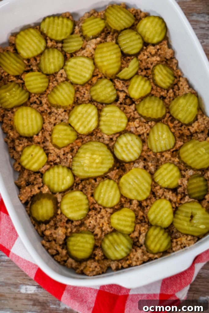Loaded Big Mac Tater Tot Bake 8 Browned ground beef is evenly spread in the bottom of a white baking dish. Pickle slices are evenly placed on top.