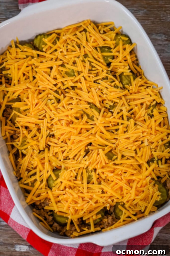 Loaded Big Mac Tater Tot Bake 9 Ground beef and pickles are topped with shredded cheddar cheese in a white baking dish.
