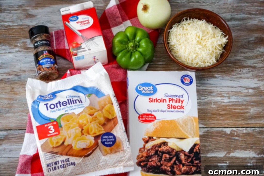 Cheesesteak Stuffed Tortellini 3 Montreal steak seasoning, heavy whipping cream, a green bell pepper, an onion, shredded provolone cheese, seasoned Sirloin Philly Steak, and a bag of frozen Cheese Tortellini on a red and white checked handkerchief.