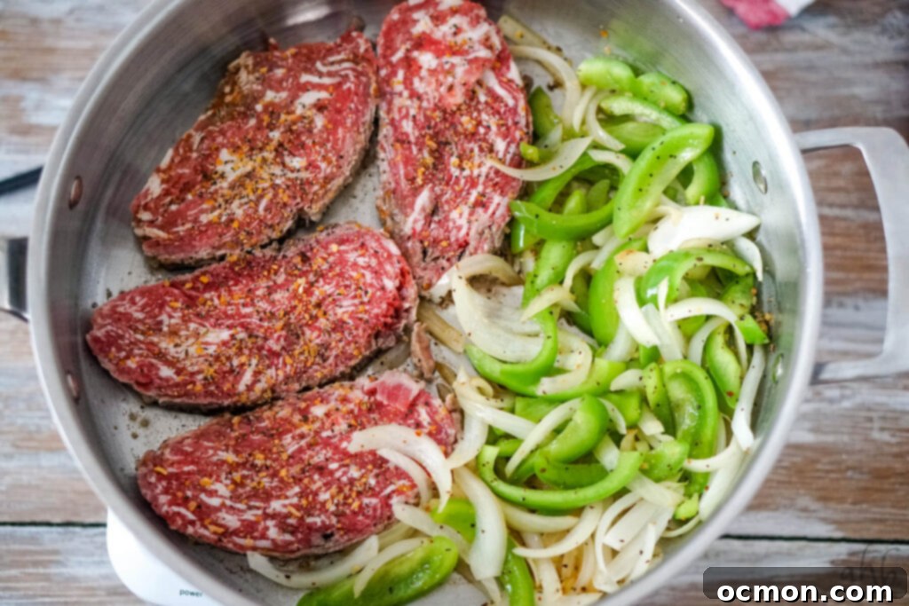 Cheesesteak Stuffed Tortellini 4 Four steaks cook in a sauté pan with slices of green pepper and onion.