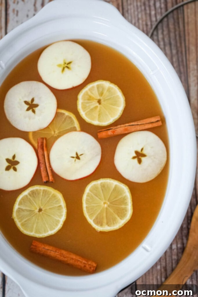 Sunburst Cider 5 Lemonade Cider in a white crockpot with sliced apples, lemons and cinnamon sticks floating on top.