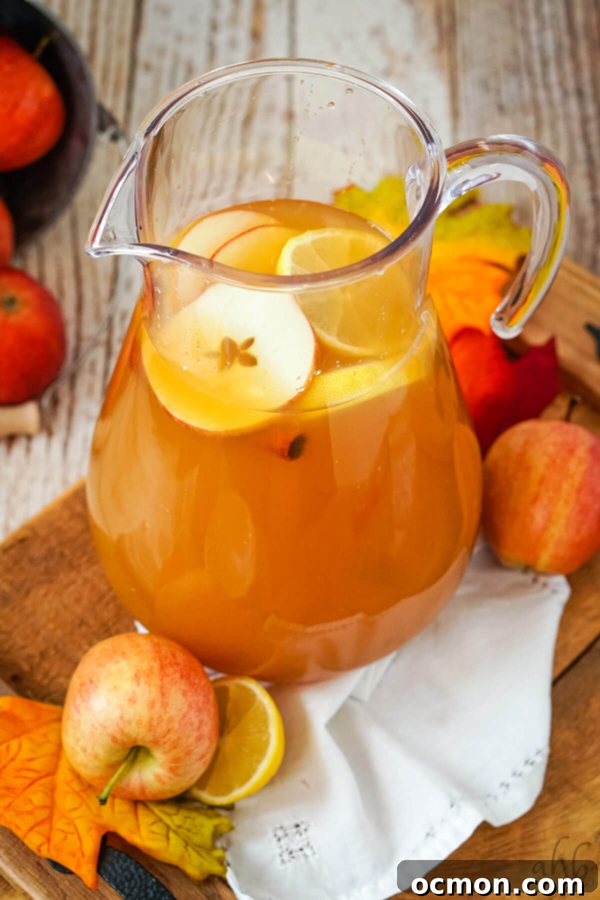 Sunburst Cider 6 A glass pitcher full of Lemonade Cider garnished with sliced apples, lemons, and cinnamon sticks surrounded by apples.